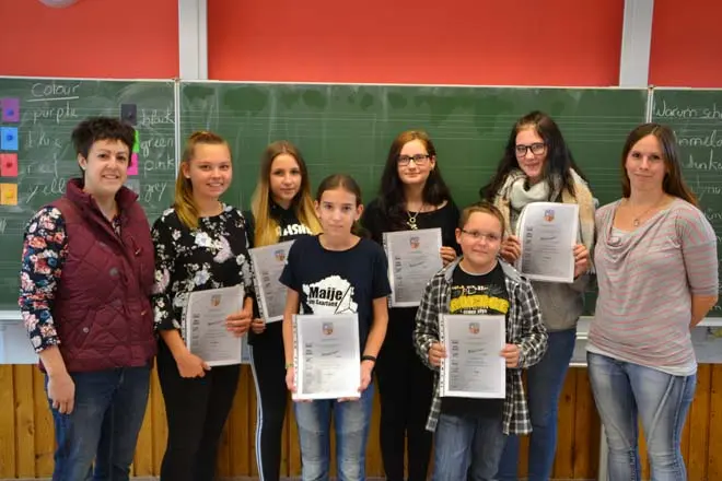 Sieben Schülerinnen und Schüler mit Urkunden zwischen zwei Frauen vor einer Tafel