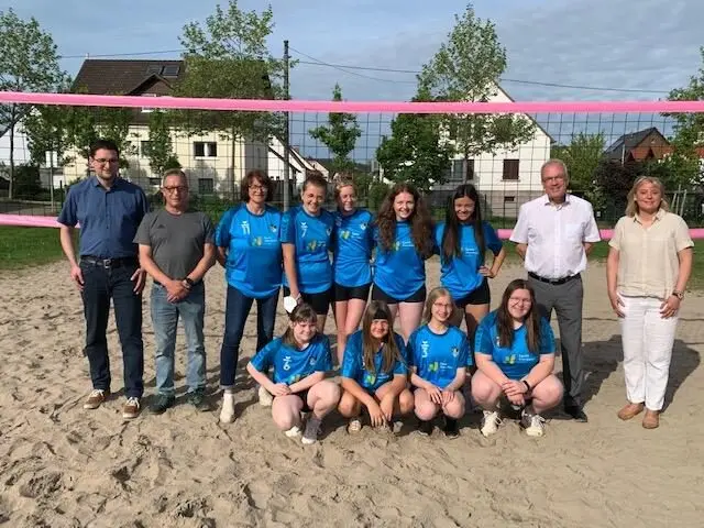 Volleyballmannschaft in blauen Trikots mit Erwachsenen auf einem Beachvolleyballfeld vor dem Netz
