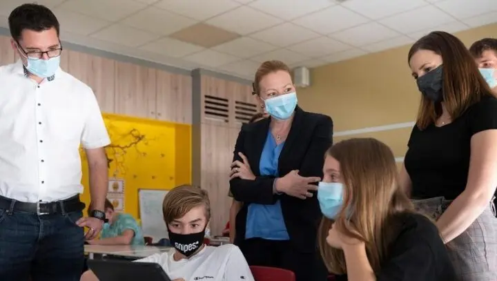 Erwachsene mit Masken schauen Jugendlichen bei der Arbeit am Tablet im Klassenraum zu