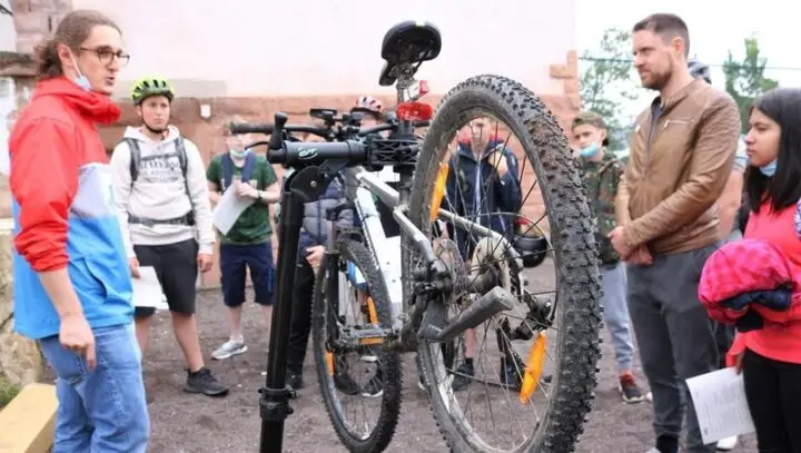 Ein Fahrrad im Montageständer, drumherum Jugendliche und Erwachsene, eine Person erklärt