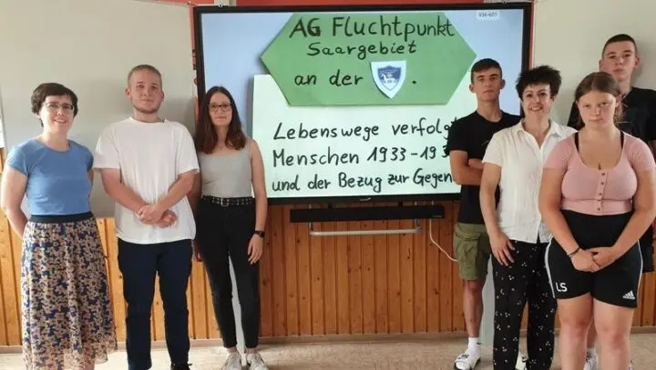 Sieben Personen vor einem Bildschirm mit „AG Fluchtpunkt Saargebiet“ und „Lebenswege verfolgter Menschen“