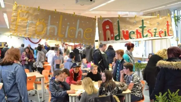 Adventsbasar: voller Raum unter Bannern „Fröhliche Adventszeit“, Besucher an Tischen