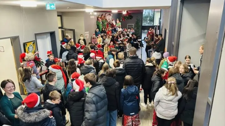 Viele Schülerinnen und Schüler, teils mit Weihnachtsmützen, beim Adventssingen im Foyer