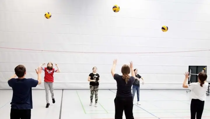 Schülerinnen und Schüler spielen sich in der Sporthalle Volleybälle zu