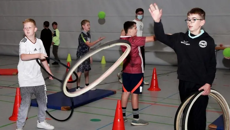 Schülerinnen und Schüler werfen in der Turnhalle Reifen und Bälle