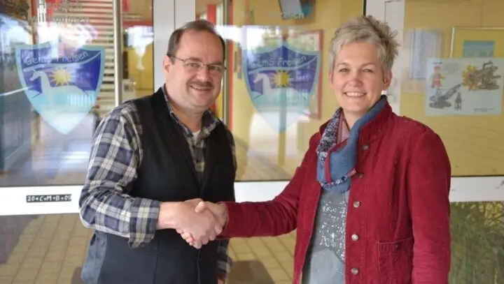 Ein Mann und eine Frau geben sich vor dem Schuleingang mit dem Logo der GemS Freisen die Hand