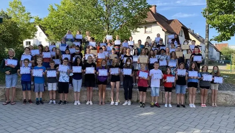 Große Gruppe von Schülerinnen und Schülern hält im Freien Urkunden hoch