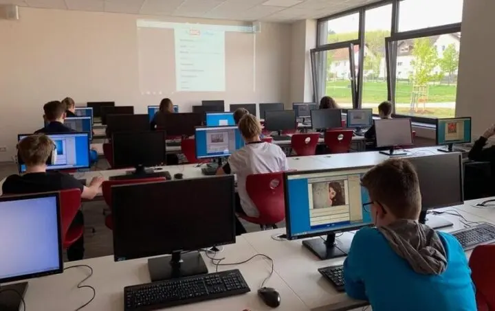 Schülerinnen und Schüler arbeiten an Computern in einem Computerraum, vorne eine Projektion