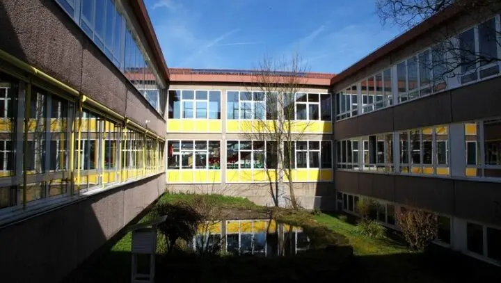 Innenhof des Schulgebäudes mit gelben Fensterbändern und kleinem Teich