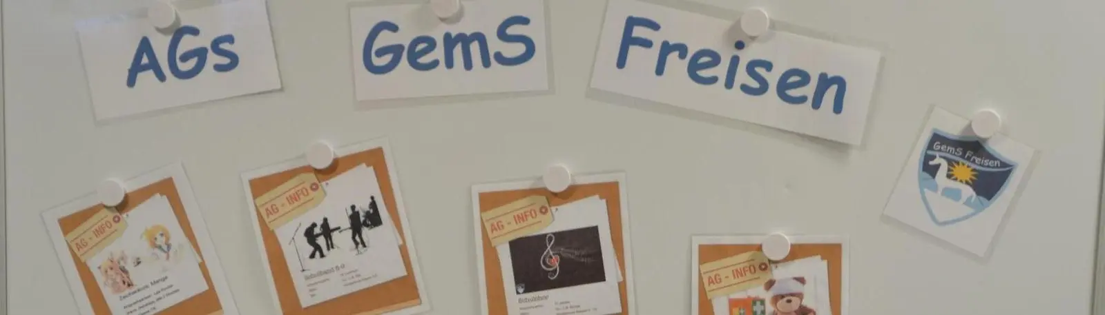 Pinnwand mit der Überschrift „AGs GemS Freisen“, AG-Infozetteln und Schulwappen