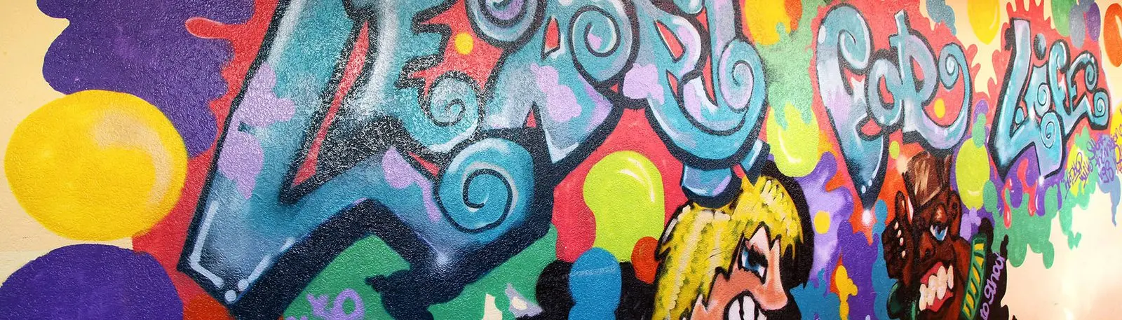 Buntes Graffiti an einer Wand mit geschwungenem Schriftzug und zwei Comicfiguren