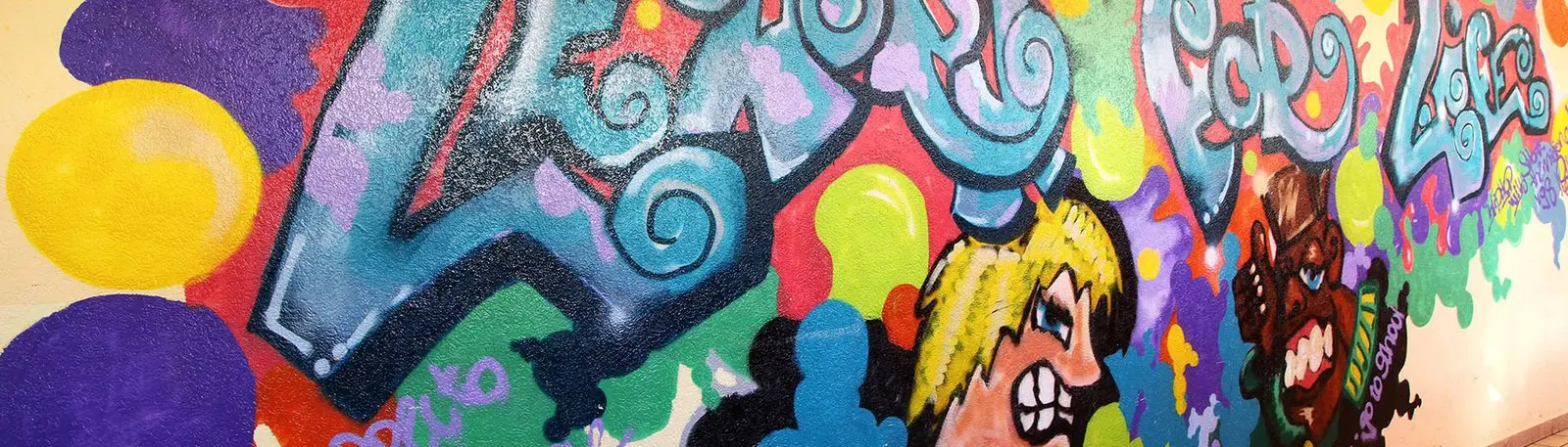 Buntes Graffiti an einer Wand mit geschwungenem Schriftzug und zwei Comicfiguren
