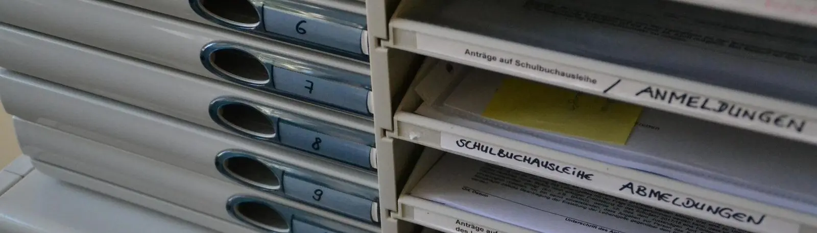 Ablagefächer, beschriftet mit Anmeldungen und Abmeldungen zur Schulbuchausleihe