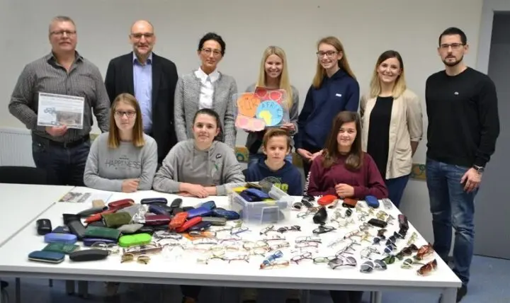 Gruppe hinter einem Tisch voller gesammelter Brillen und Etuis, ein Schild „Für Afrika“