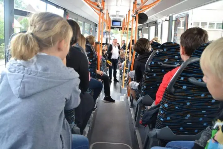 Kinder sitzen im Bus, vorne im Gang steht ein Mitarbeiter und erklärt