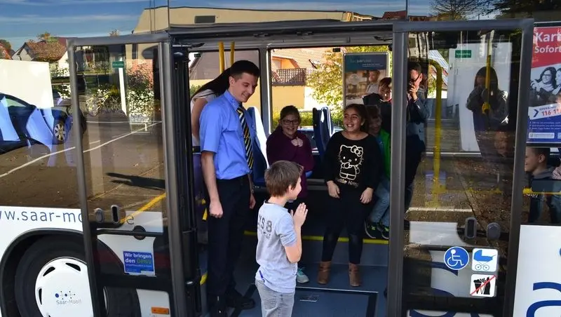 Kinder stehen in der offenen Tür eines Saar-Mobil-Busses, davor ein Busfahrer und ein Junge