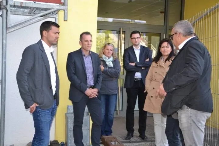 Sechs Erwachsene stehen im Gespräch vor dem Eingang eines Gebäudes neben einem Baugerüst
