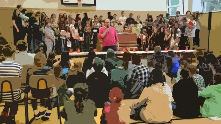Mann mit Mikrofon vor dem Schulchor, Schülerinnen und Schüler sitzen davor auf dem Boden, grafisch verfremdet