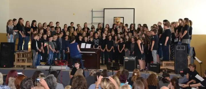 Großer Chor auf der Bühne der Turnhalle mit Klavier und Verstärkern, im Vordergrund das Publikum