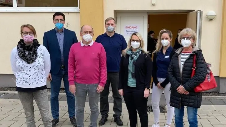 Sieben Erwachsene mit FFP2-Masken vor dem Eingang mit Schild „Eingang Testzentrum“