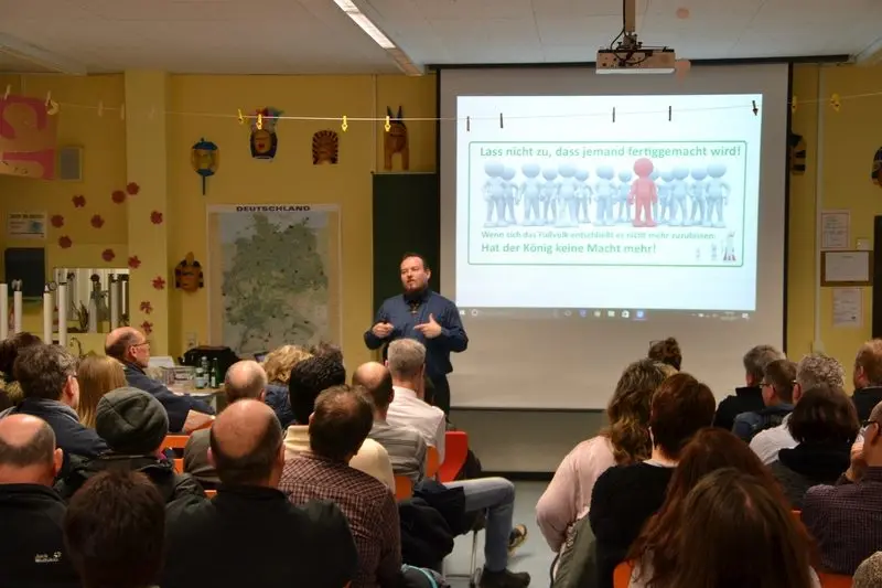 Referent spricht vor Eltern, auf der Leinwand: „Lass nicht zu, dass jemand fertiggemacht wird!“