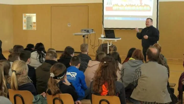 Referent spricht vor einer Projektion zu Cybermobbing zu Schülerinnen und Schülern in der Turnhalle
