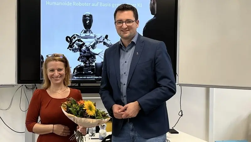 Frau mit Blumenstrauß und Mann vor einer Präsentationsfolie „Humanoide Roboter auf Basis generativer KI“