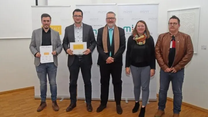Fünf Erwachsene vor MINT-Aufstellern, zwei halten Urkunden „Digitale Schule“