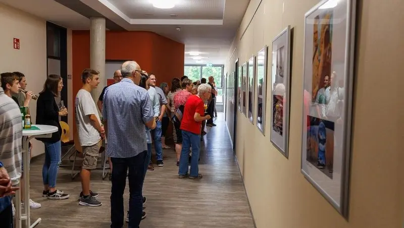 Besucherinnen und Besucher in einem Flur betrachten gerahmte Fotos an der Wand