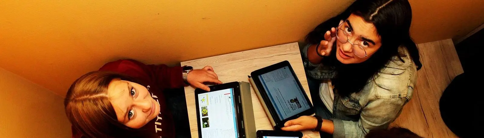 Zwei Schülerinnen mit Tablets an einem Tisch, von oben fotografiert