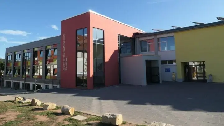 Moderner Schulbau mit roter Fassade und Schriftzug „Gemeinschaftsschule Freisen“ bei Sonne