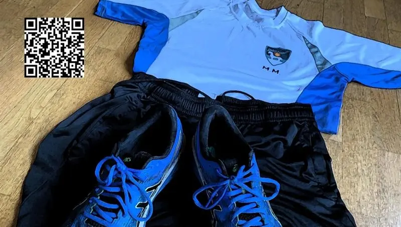 Sportshirt, Sporthose und Laufschuhe auf Holzboden, daneben ein QR-Code
