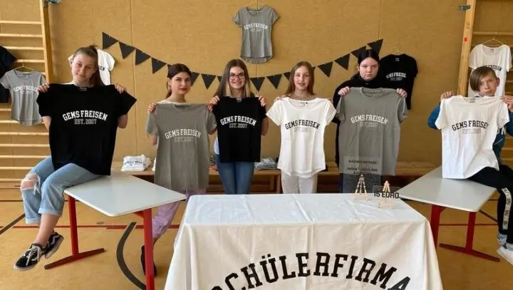 Schülerinnen und Schüler halten T-Shirts „GemS Freisen Est. 2007“ hinter Verkaufstisch