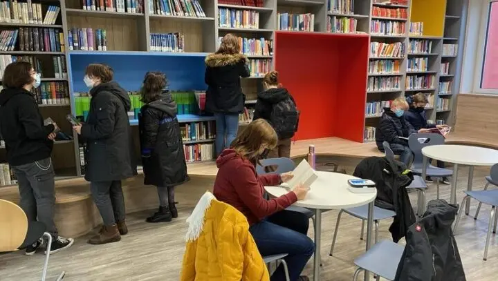 Schülerinnen und Schüler mit Masken stöbern in den Regalen der neuen Schulbibliothek, eine liest am Tisch