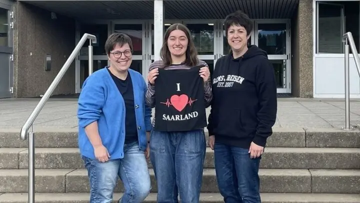 Drei Frauen auf der Schultreppe, die mittlere hält eine Stofftasche mit der Aufschrift „I ♥ Saarland“