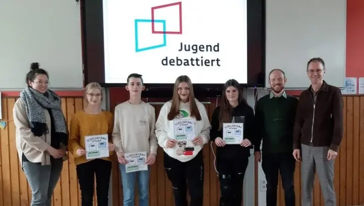 Vier Jugendliche mit Gutscheinen und drei Erwachsene vor einer Leinwand mit „Jugend debattiert“-Logo