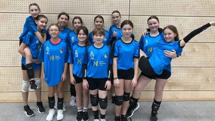 Mädchen-Volleyballteam in blauen Trikots in einer Sporthalle, zwei Spielerinnen werden huckepack getragen