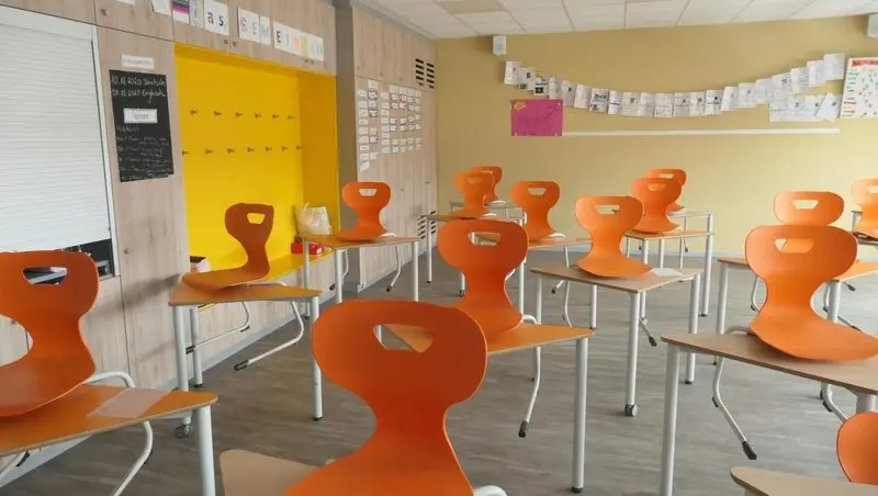 Leerer Klassenraum mit orangefarbenen Stühlen, die hochgestellt auf den Tischen stehen