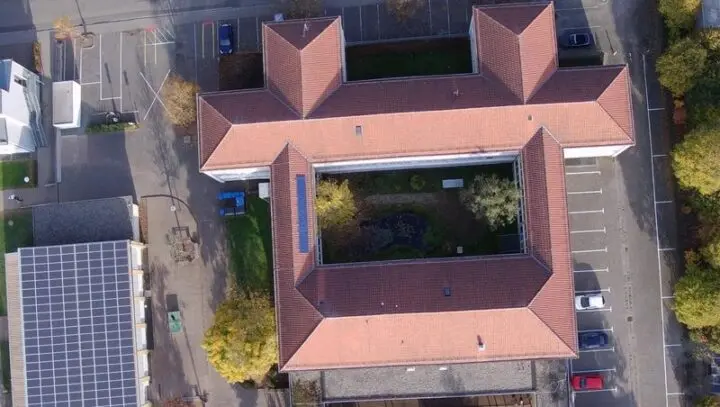 Luftaufnahme von oben auf das Schulgebäude mit Innenhof und Parkplätzen