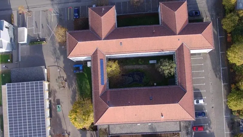 Luftaufnahme von oben auf das Schulgebäude mit Innenhof und Parkplätzen
