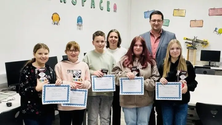 Fünf Schülerinnen und Schüler mit Urkunden und Speed-Cubes, dahinter zwei Erwachsene in einem Computerraum