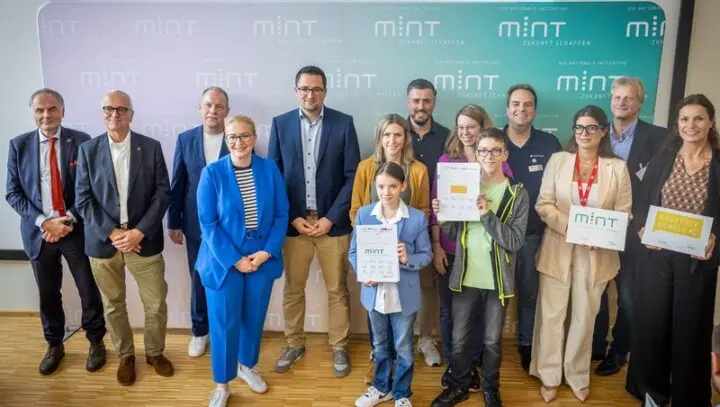 Gruppe vor einer MINT-Wand, zwei Jugendliche und Erwachsene halten Urkunden „MINT“ und „Digitale Schule“