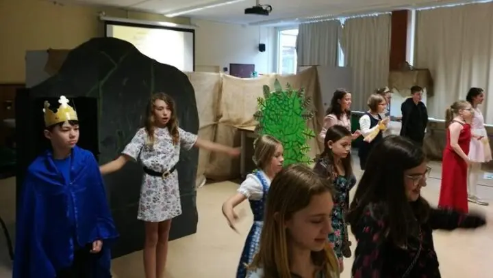 Kostümierte Kinder, eines mit Krone und blauem Umhang, spielen vor gemalter Kulisse Theater
