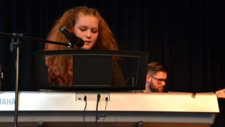 Schülerin singt am Keyboard auf der Bühne ins Mikrofon