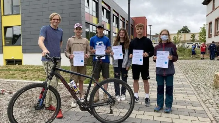 Sechs Jugendliche mit Urkunden und ein Mann mit Mountainbike vor dem Schulgebäude
