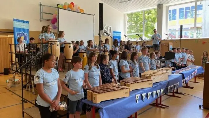MusiKlasse in hellblauen T-Shirts mit Xylofonen und Trommeln beim Konzert in der Turnhalle