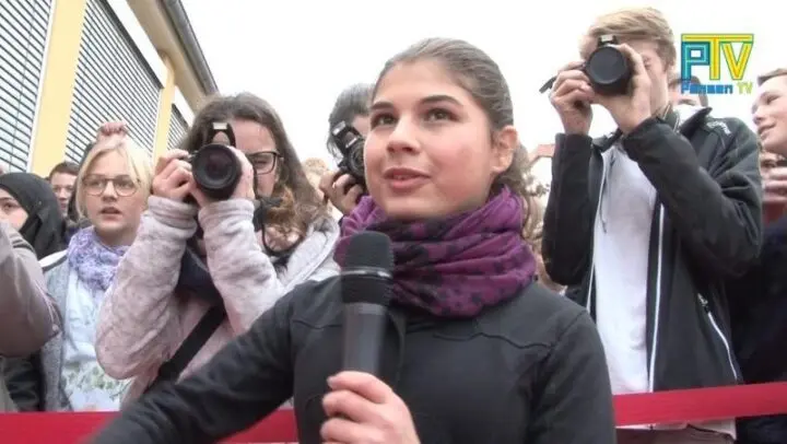 Jugendliche spricht ins Mikrofon, dahinter Personen mit Kameras, Logo „PTV Pensen TV“