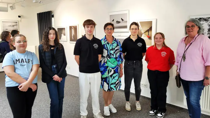 Jugendliche und Erwachsene stehen in einem Ausstellungsraum vor gerahmten Fotos