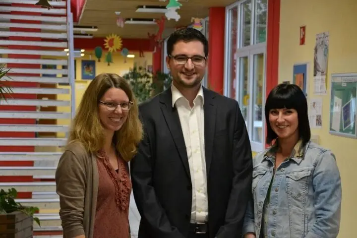 Ein Mann und zwei Frauen stehen lächelnd in einem Schulflur