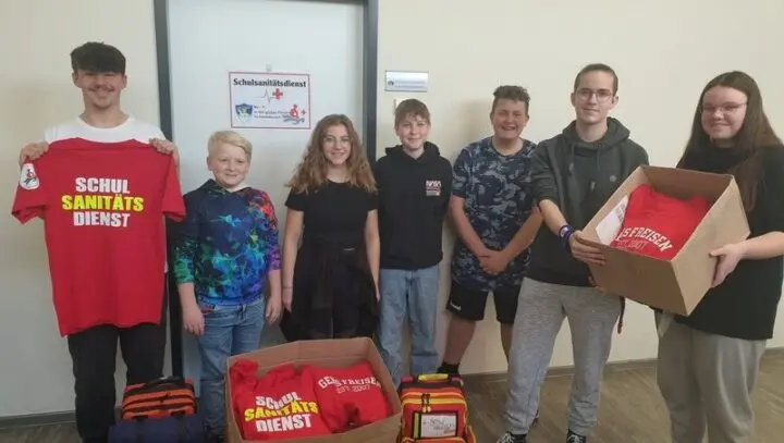 Sieben Jugendliche mit neuen roten Shirts „Schulsanitätsdienst“ und Kartons